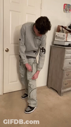 Man In Grey Sweatshirt And Cargo Pants Standing In Front Of Door GIF