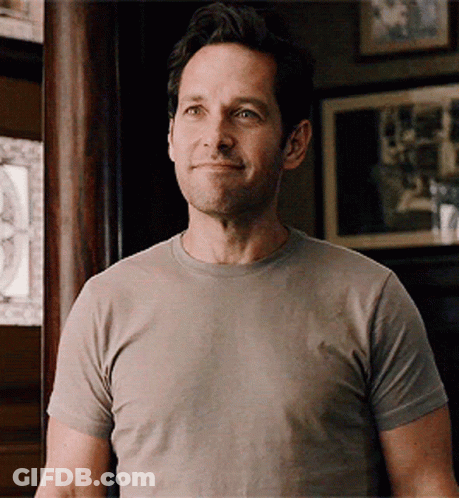 Man In Grey T-Shirt Smiling In Front Of Picture Wall GIF