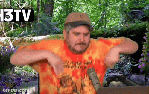Man In Hat And Orange Shirt Talking Into Microphone In Front Of 13 TV Sign GIF