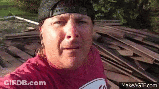 Man In Hat And Red Shirt Next To Wood Pile GIF
