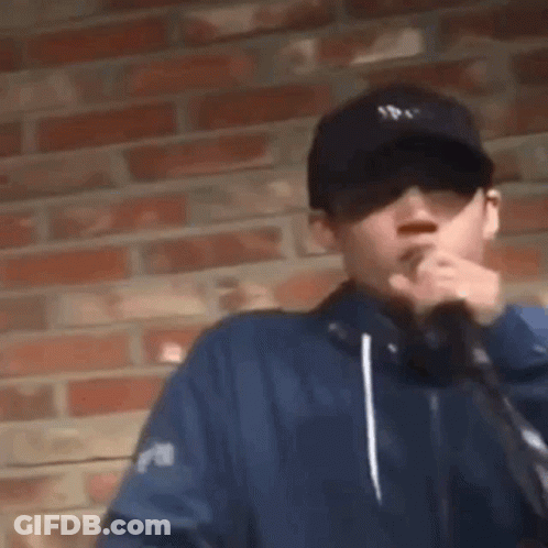 Man In Hat And Sunglasses Smoking By Brick Wall GIF