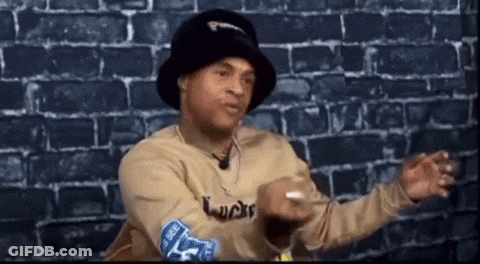 Man In Hat And Sweater Sitting By Brick Wall Talking GIF