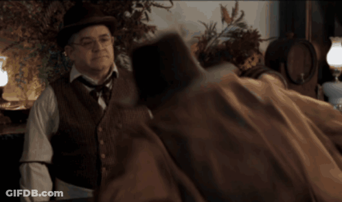 Man In Hat And Vest Talking To Man In Brown Coat GIF
