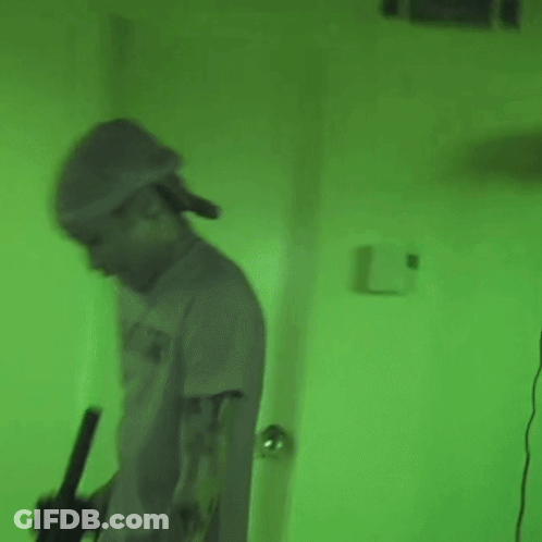 Man In Hat Holding Gun In Green Lit Room GIF