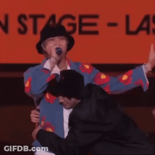 Man In Hat Hugging Man In Front Of Stage Sign GIF