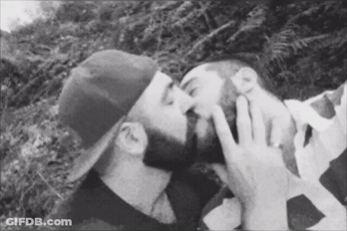Man In Hat Kissing Another Man On Cheek GIF