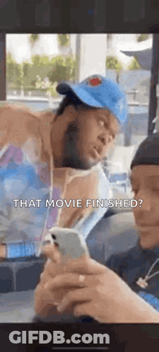Man In Hat Looking At Phone While Another Watches GIF