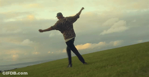 Man In Hat On Grassy Hill With Arms Outstretched GIF