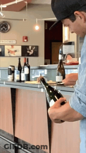 Man In Hat Opening Wine In Front Of Tomorrow Sign GIF
