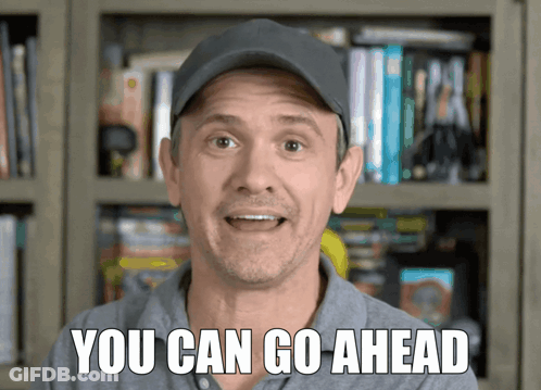 Man In Hat Saying You Can Go Ahead In Front Of Bookshelf GIF