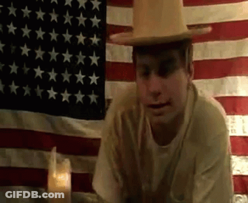 Man In Hat Sitting In Front Of American Flag GIF