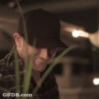 Man In Hat Smiling And Thumbs Up Next To Plant GIF