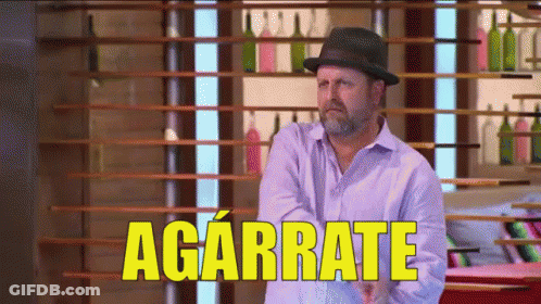 Man In Hat Standing Before Agárrate Sign GIF