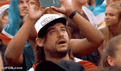 Man In Hat Taking Selfie In Crowd GIF
