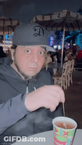 Man In Hat With Letter D Sitting At Table With Disneyland Drink GIF