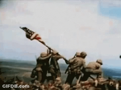 Man In Hat With Letter R Standing Before Flag GIF