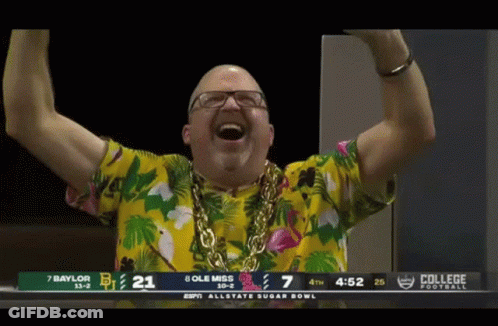 Man In Hawaiian Shirt And Gold Chain In Front Of College Football Scoreboard GIF