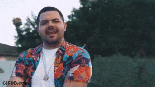 Man In Hawaiian Shirt And Necklace Standing In Front Of Trees GIF