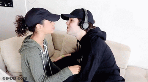 Man In Headphones And Baseball Cap Kissing Woman On Cheek GIF