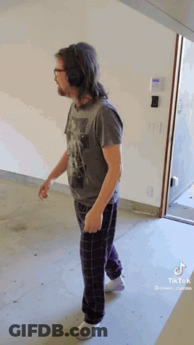 Man In Headphones And Pajama Pants Walking In Hallway GIF