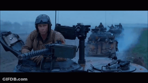 Man In Helmet Holding Machine Gun In Front Of Tanks GIF