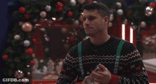 Man In Ho Ho Ho Sweater Holding Glass By Christmas Tree GIF