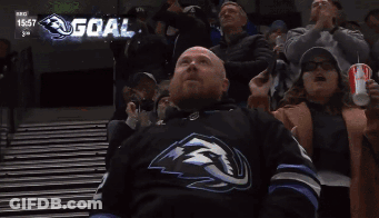 Man In Hockey Jersey Laying On Bleachers Watching Game With Scoreboard Showing Goal GIF