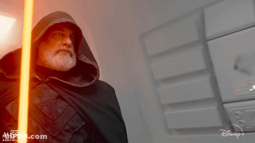 Man In Hooded Cape Holding Lightsaber In Front Of Ahsoka Sign GIF