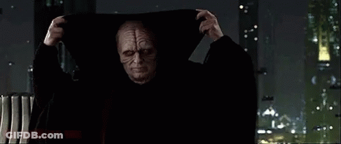Man In Hooded Cloak By Window In Dark Room GIF