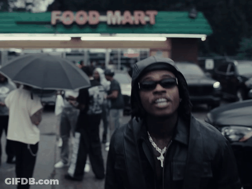 Man In Hooded Jacket In Front Of Food Mart GIF