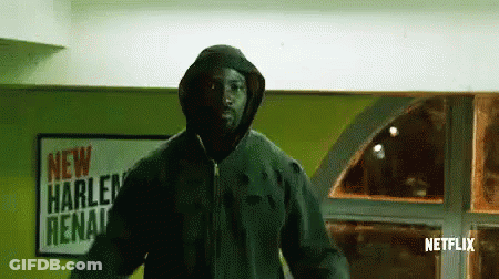 Man In Hooded Jacket In Front Of New Harlem Arena Sign GIF