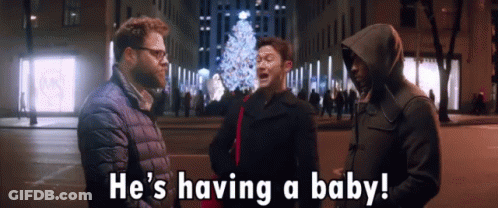 Man In Hooded Jacket Says Having A Baby In Front Of Christmas Tree GIF