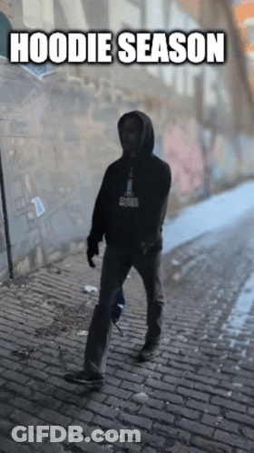 Man In Hoodie Walking Down Cobblestone Street GIF