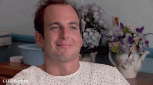 Man In Hospital Gown Smiling Beside Flowers GIF