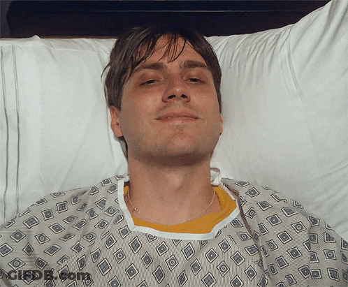 Man In Hospital Gown Smiling In Bed GIF
