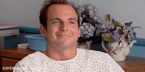 Man In Hospital Gown Smiling With Flowers GIF