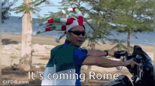 Man In Jester Hat And Sunglasses Saying It's Coming Rome On Beach GIF