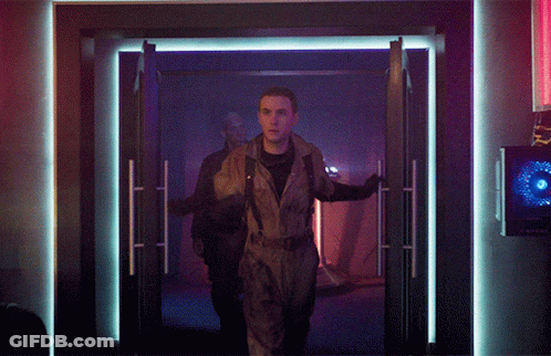 Man In Jumpsuit Walking Through Doorway In Dark Room GIF