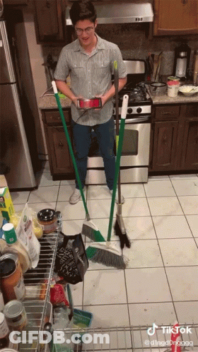 Man In Kitchen Holding Broom And Phone GIF