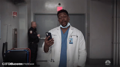 Man In Lab Coat Holding Cell Phone In Front Of NBC Sign GIF