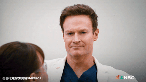 Man In Lab Coat Talking To Woman With NBC Logo GIF