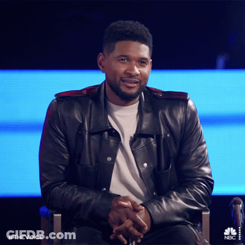 Man In Leather Jacket Sitting With Hands Folded In Front Of NBC Screen GIF