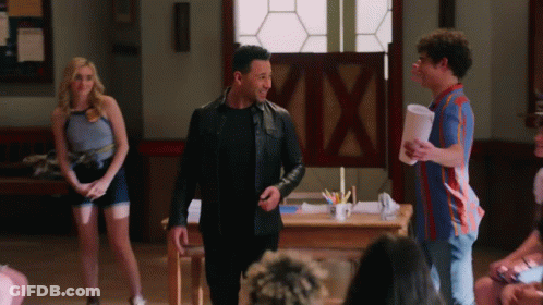 Man In Leather Jacket Standing In Front Of Group Talking To Another Man GIF