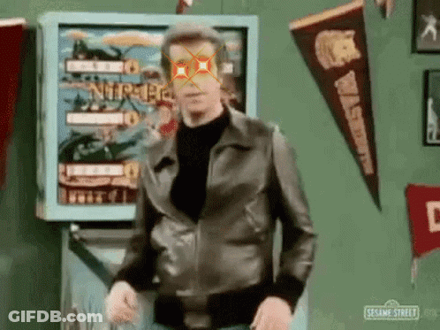 Man In Leather Jacket Standing In Front Of Pinball Machine With Red Eye GIF