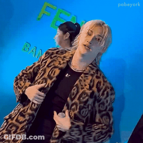 Man In Leopard Print Coat Holding Microphone And Woman With Ponytail GIF