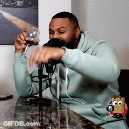 Man In Light Blue Sweatshirt Holding Wine Glass At Microphone GIF