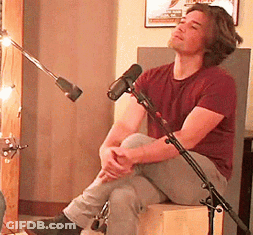 Man In Maroon Shirt Sitting On Box By Microphone GIF