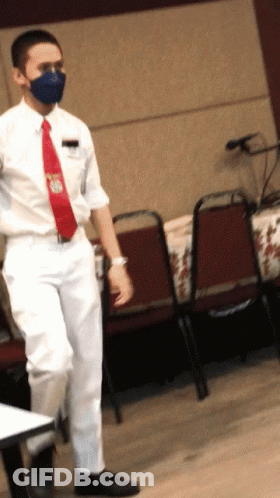 Man In Mask And Red Tie Standing At Table GIF