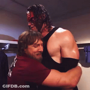 Man In Mask Hugging Man In Maroon Shirt GIF