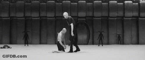 Man In Mask Kneeling Next To Another Man In Black And White Photo GIF